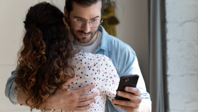 husband hugging wife and looking at phone